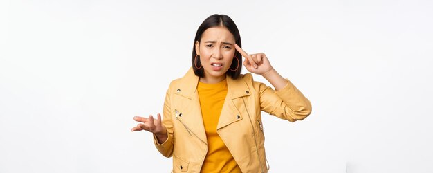 Annoyed asian woman roll finger near temple and staring frustrated scolding someone stupid or crazy standing over white background