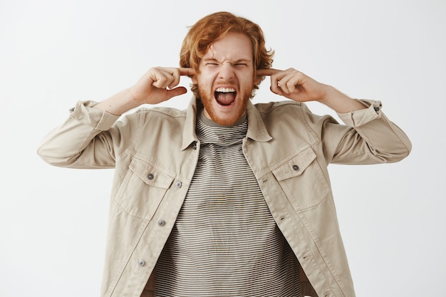 Annoyed bearded redhead guy posing against the white wall