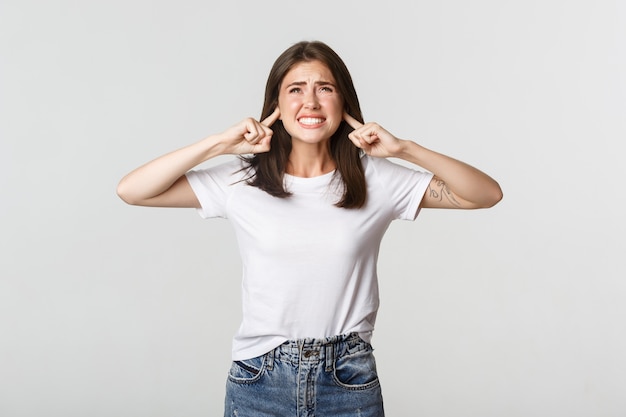 Annoyed and bothered girl shut ears and complaining at loud awful noise.