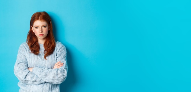 Foto gratuita ragazza rossa infastidita e infastidita incrocia le braccia sul petto fissando qualcosa di noioso e noioso