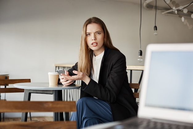 Free photo annoyed businesswoman sit in cafe with mobile phone and looking at person irritated