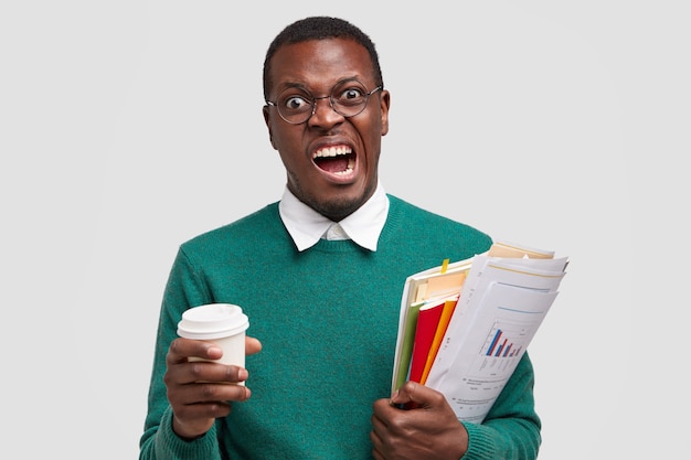 Annoyed dark skinned male frowns face, doesnt want to study economy, market, money and tax, being investment consultant, analyzes company annual report