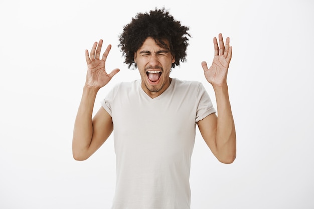 Free photo annoyed and distressed dark-skinned man raising hands up and screaming