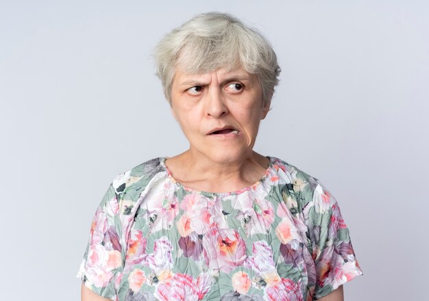 Annoyed elderly woman looks at side isolated on white wall