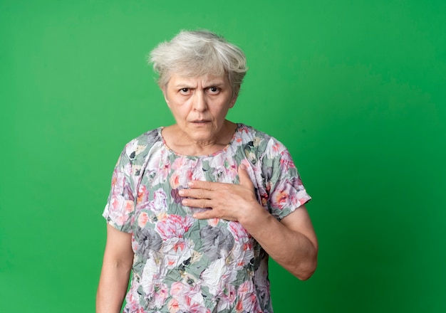 イライラする年配の女性はあごに手を置き、緑の壁に孤立して見える