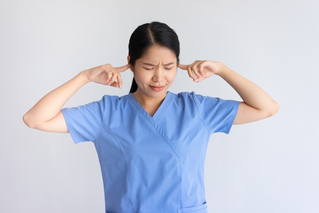 Annoyed female doctor stopping ears with fingers