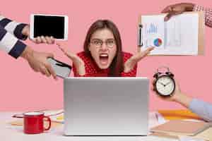 Free photo annoyed freelancer gestures in front of laptop computer, has much paperwork, works overtime, cries desperately