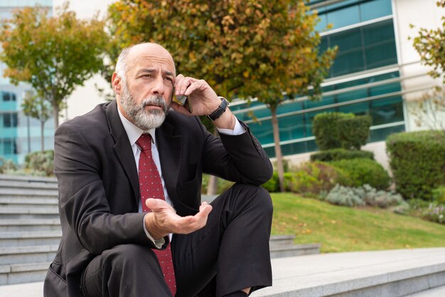 Annoyed grey haired businessman talking on phone
