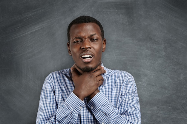 Free photo annoyed grumpy young african teacher or student in casual shirt holding himself for neck, making suicide gesture, as if trying to drown or choke himself, showing his irritated and fed-up attitude