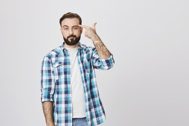 Annoyed and indifferent man make finger gun, shooting himself from boredom