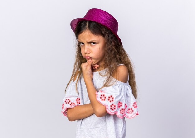 раздраженная маленькая кавказская девушка с фиолетовой шляпой, держащая подбородок на белой стене с копией пространства