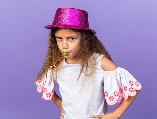 раздраженная маленькая кавказская девушка с фиолетовой шляпой дует свисток на фиолетовой стене с копией пространства