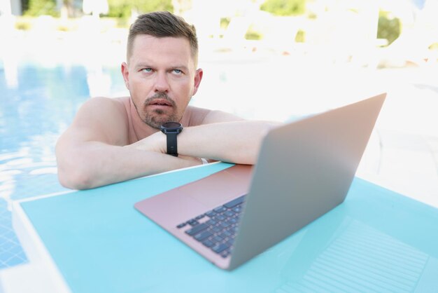 Annoyed man working on a laptop from the pool