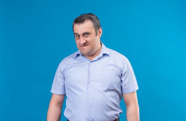 Annoyed middle-aged man in blue shirt looking at the camera with displeased expression on a blue space