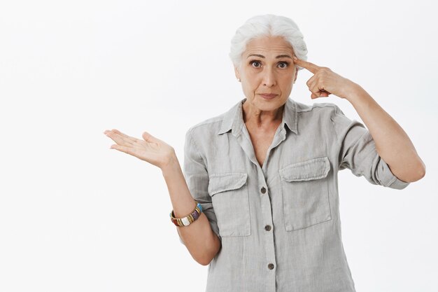 Annoyed old lady pointing finger at forehead, scolding person acting crazy