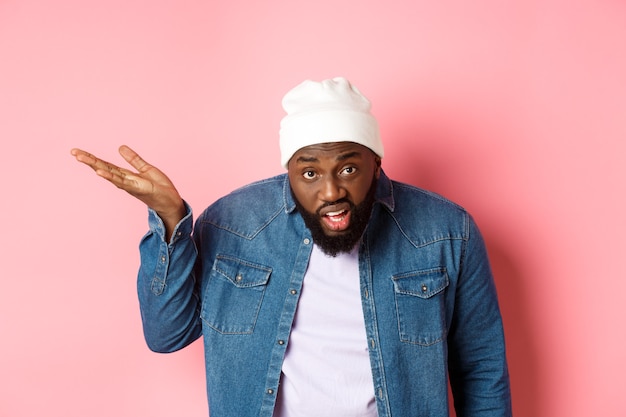 Annoyed and pissed-off Black man arguing, staring at camera and scolding person, standing over pink background