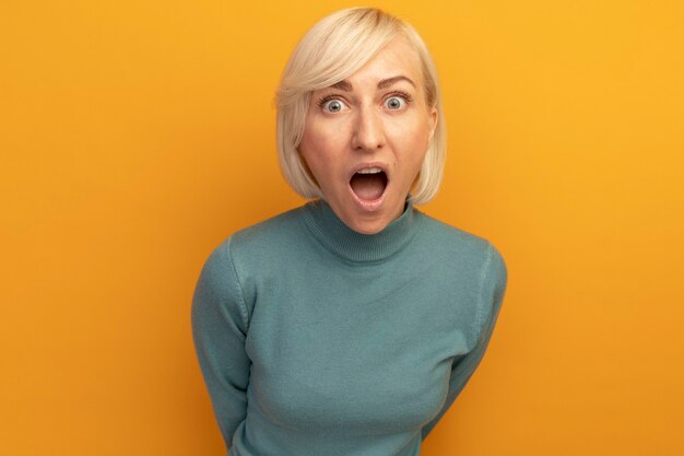 Annoyed pretty blonde slavic woman yells at someone looking at front isolated on orange wall