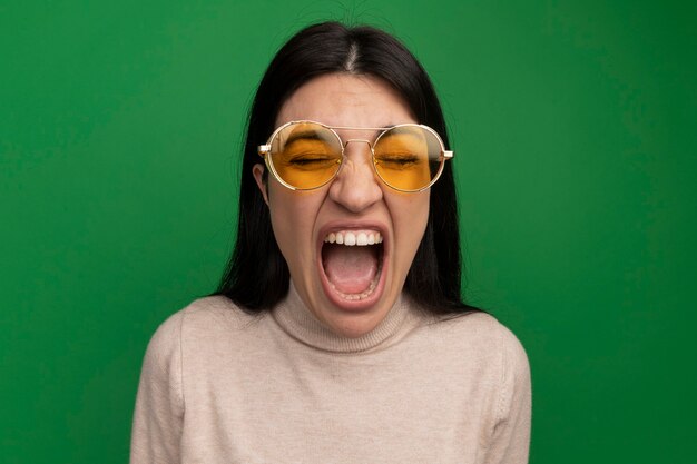 Free photo annoyed pretty brunette caucasian girl in sun glasses screams on green