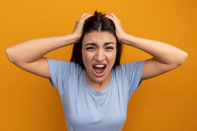 Annoyed pretty brunette woman holds head isolated on orange wall