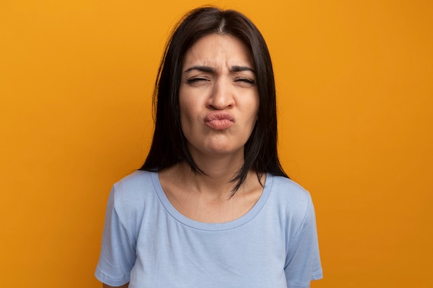 Annoyed pretty brunette woman looks at front isolated on orange wall