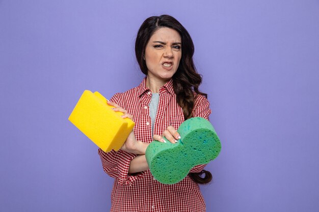 Annoyed pretty caucasian cleaner woman crossing her hands and holding sponges 