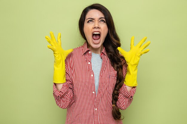 Раздраженная симпатичная кавказская уборщица в резиновых перчатках держит руки открытыми и смотрит вверх