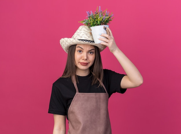 ピンクの頭の上に植木鉢を保持しているガーデニング帽子をかぶっているイライラするかなり白人女性の庭師