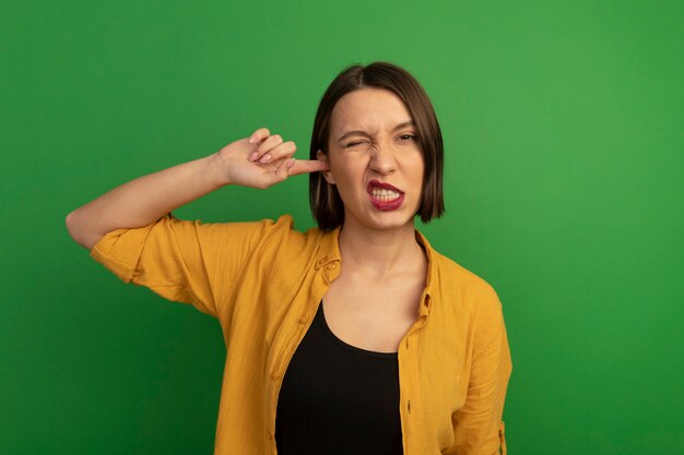 Annoyed pretty caucasian woman closes ear with finger on green