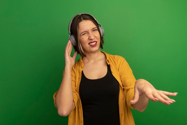 Annoyed pretty caucasian woman on headphones holds hand open isolated