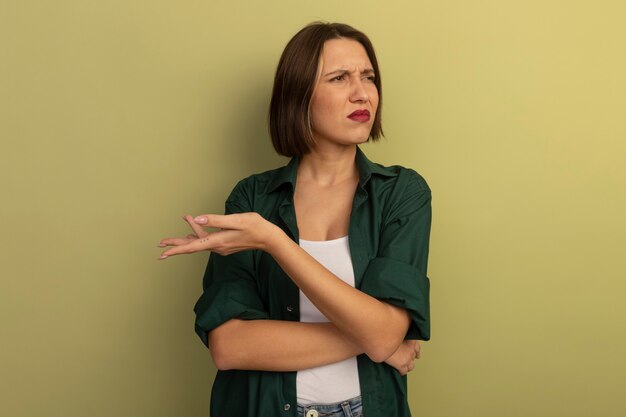 Annoyed pretty woman holds hand open and looks at side isolated on olive green wall