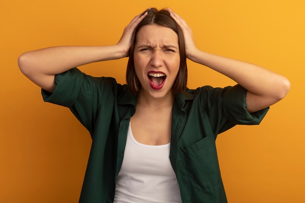 Foto gratuita la donna graziosa infastidita tiene la testa isolata sulla parete arancione