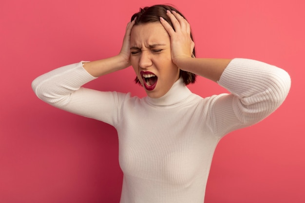 Free photo annoyed pretty woman holds head isolated on pink wall