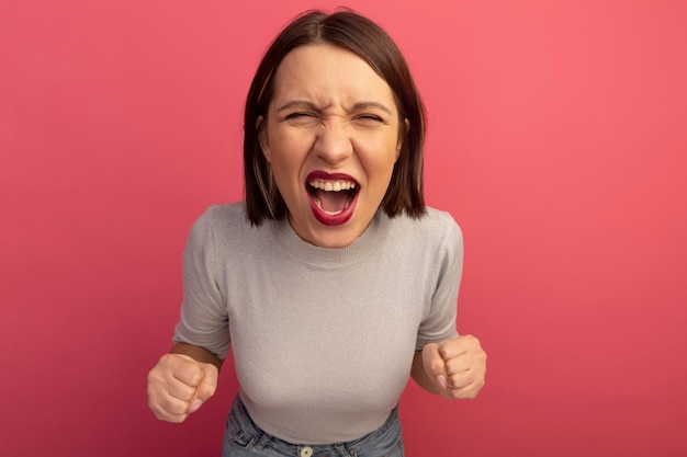 Foto gratuita la donna graziosa infastidita tiene i pugni e le urla isolati sulla parete rosa