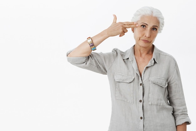 Free photo annoyed senior lady making shot gun gesture over forehead