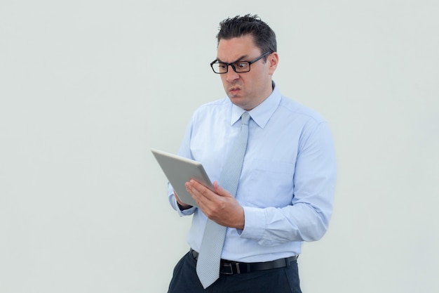 Annoyed shocked businessman in eyeglasses using tablet