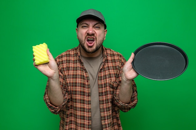 Annoyed slavic cleaner man holding dishes and sponge