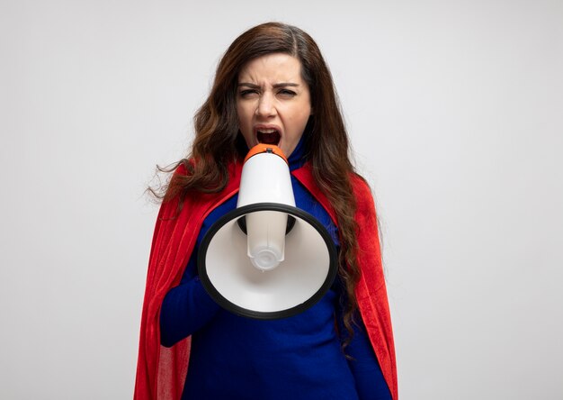 Annoyed superwoman with red cape holds and shouts into loud speaker isolated on white wall