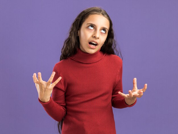 Раздраженная девочка-подросток показывает пустые руки, глядя вверх изолирована на фиолетовой стене