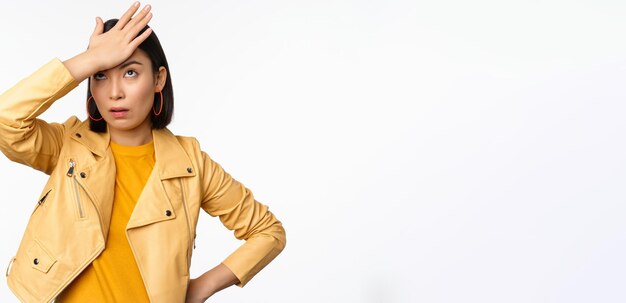 Free photo annoyed and tired asian girl slap forehead facepalm and eyeroll with bothered face expression standing in casual clothes over white studio background