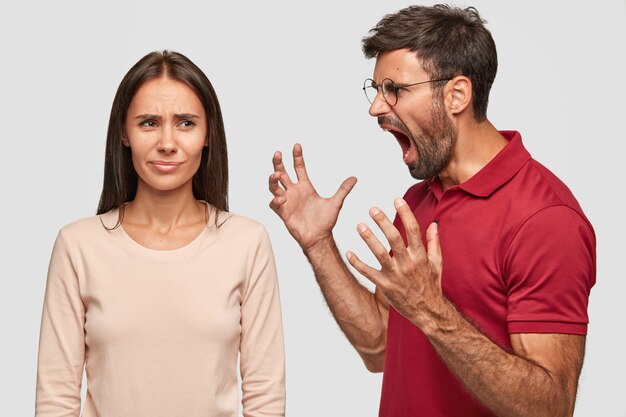 Annoyed unshaven guy gestures with hands, shouts at girlfriend, feels jeleaous, gestures angrily