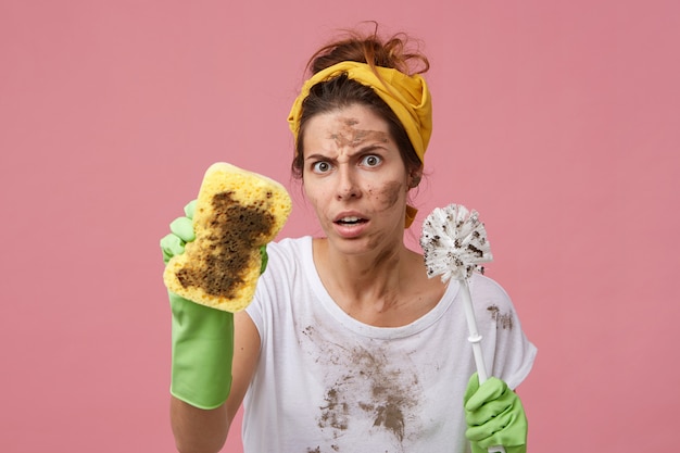 Free photo annoyed woman with dirty face holding sponge and brush in hands having bad mood