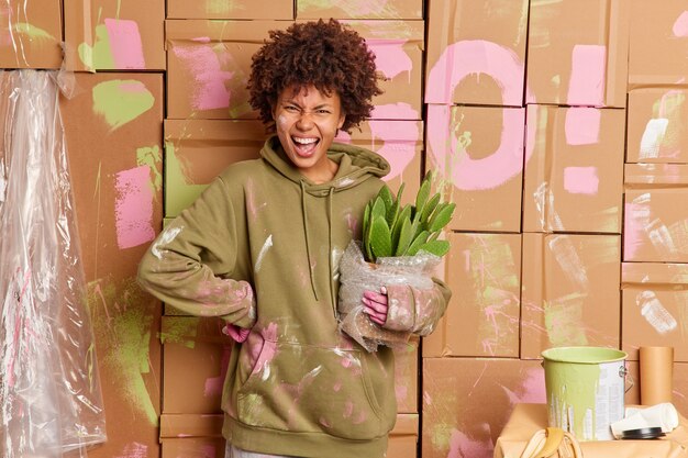 Annoyed young Afro American woman relocates in new apartment busy doing redecoration of room