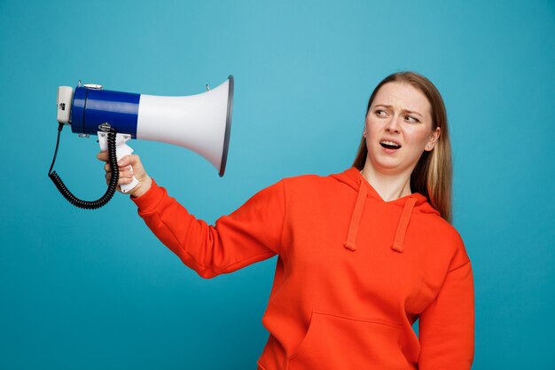 スピーカーを持って見ているイライラする若いブロンドの女性