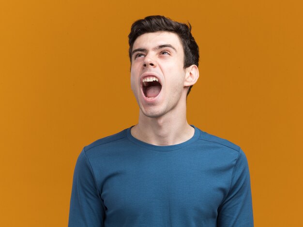 Annoyed young brunette caucasian boy yelling at someone looking up on orange