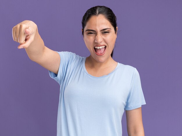 Annoyed young brunette caucasian girl looking and pointing at camera on purple