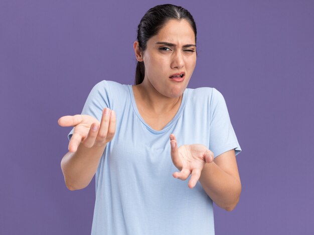 Annoyed young brunette caucasian girl looking and pointing with two hands isolated on purple wall with copy space