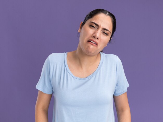 Annoyed young brunette caucasian girl looks at camera on purple