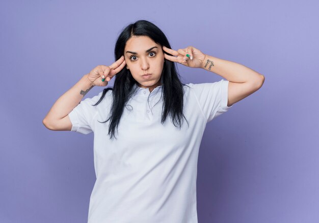 Annoyed young brunette caucasian girl puts fingers on temples looking isolated on purple wall