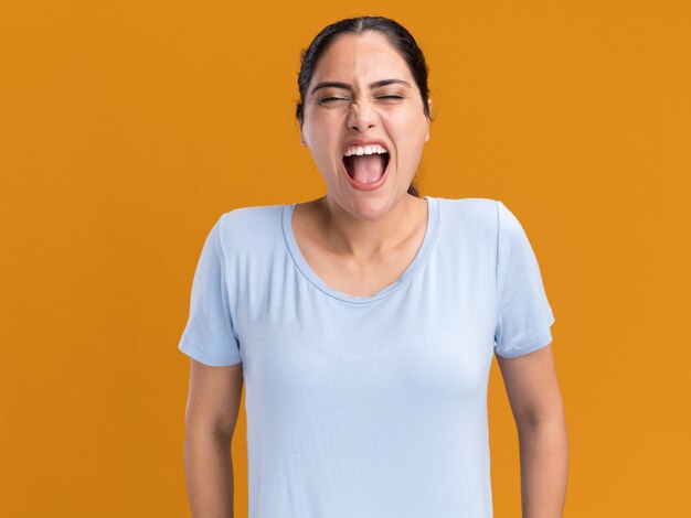 Annoyed young brunette caucasian girl screams isolated on orange wall with copy space