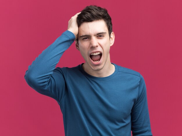 Annoyed young brunette caucasian man puts hand on head  isolated on pink wall with copy space